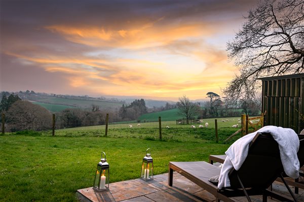 Terrace with loungers and view across fields with sunset sky.